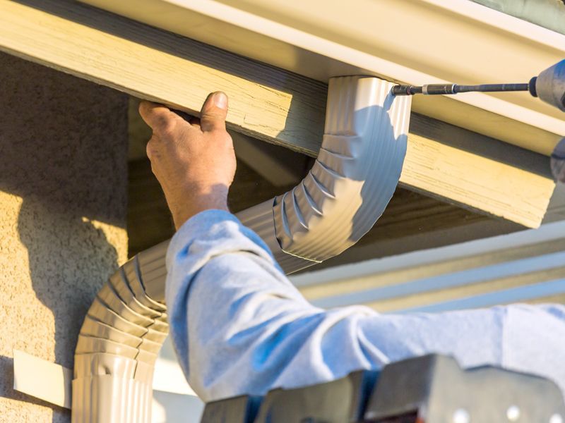 A man is installing a gutter on a house with a drill.