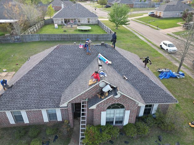 Roofers working on a residential house with brick, in a suburban setting.