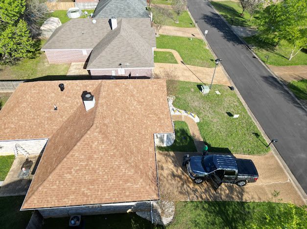 Aerial view of houses with brown roofs, a street, and a black truck parked in a driveway.