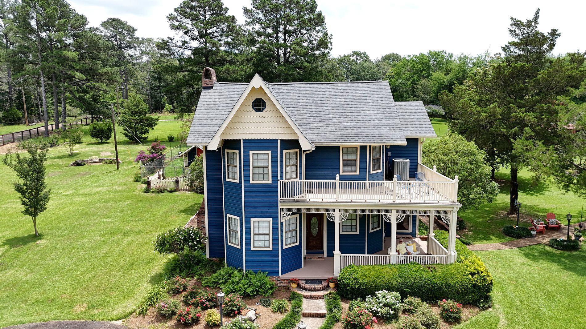 Blue Victorian house with white trim, porch, and garden on a grassy lot surrounded by trees.