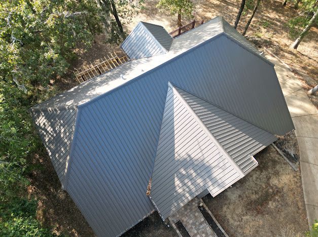 Overhead view of a gray metal roof on a house surrounded by trees in a natural setting.