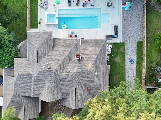 Aerial view of a house with a pool. The house has a gray roof, a pool, and a patio.