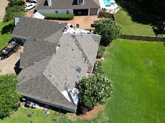 Aerial view of a house with a partially completed roof replacement, green lawn.