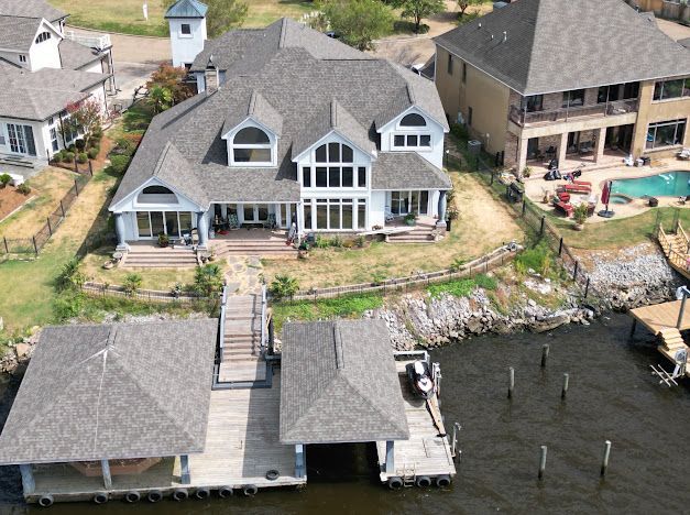 Large white house with boat docks on a lake. Grey roof, water in front, sunny day.