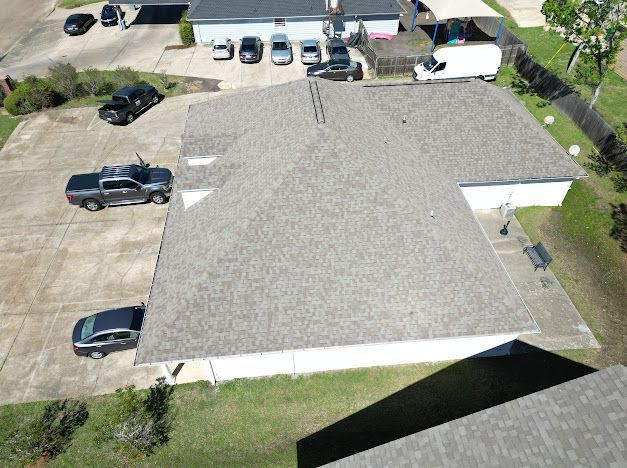 Overhead view of a house with gray shingle roof and multiple parked cars on a concrete driveway.