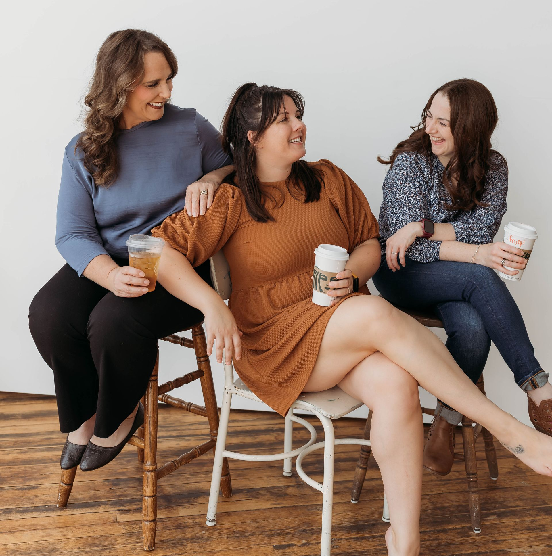 Three women seated on chairs, smiling and holding drinks.