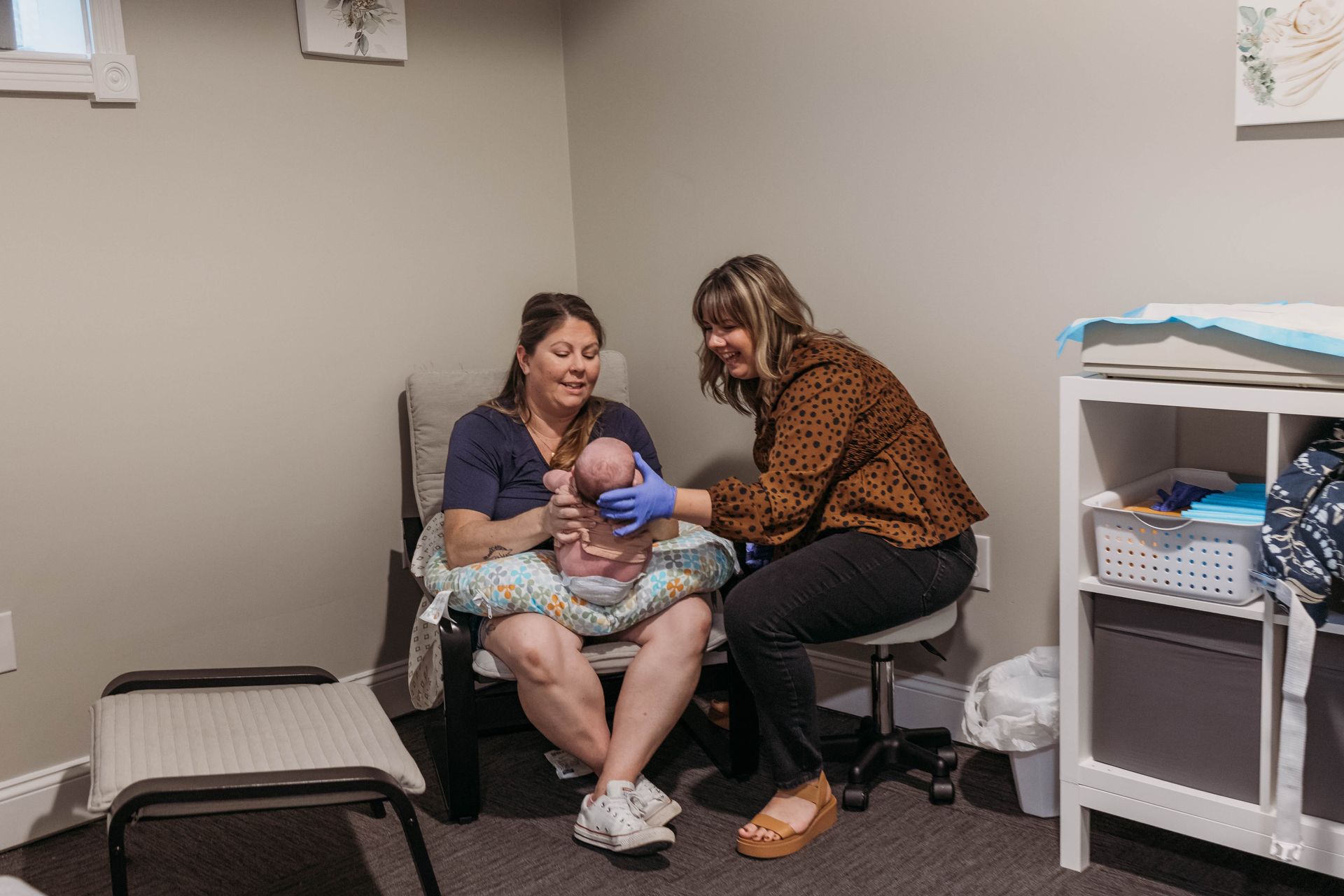 Woman holding newborn, assisted by another woman. Indoor setting.