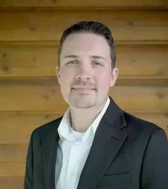 Man with dark hair and goatee smiles in a white shirt and black blazer.