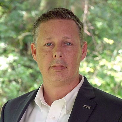 Man in a suit smiles at the camera, with a dark blue jacket, purple tie, and light blue shirt.