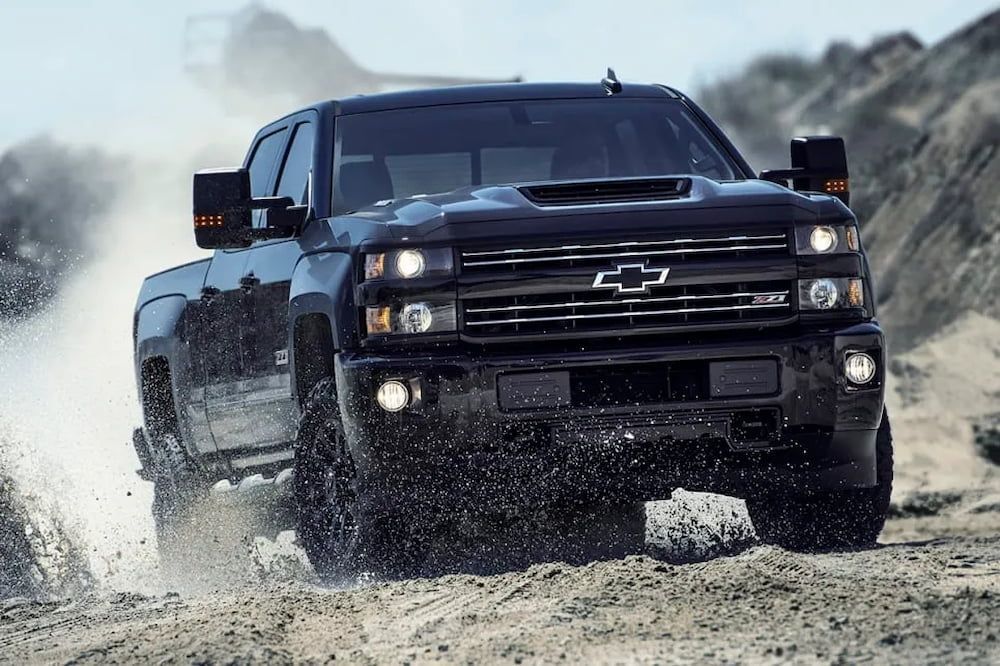 A Black Chevrolet Truck is Driving Through the Mud on a Dirt Road — Peel Valley Tyres in Murrurundi, NSW