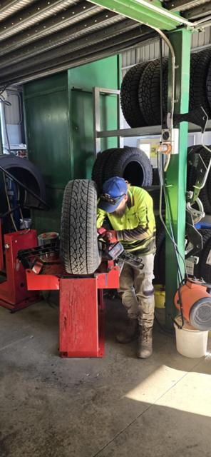A person in a workshop changing a tire on a red machine. Workshop setting. — Peel Valley Tyres in Taminda, NSW