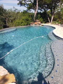 A sparkling blue pool with a stone deck, surrounded by trees under a sunny sky.