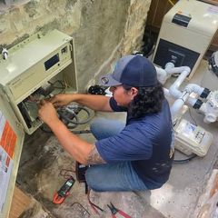 Pool technician works on electrical box, using tools. Inside setting, near pipes.