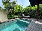 Small pool surrounded by lush greenery and a wooden deck. A lounge chair sits in the background.