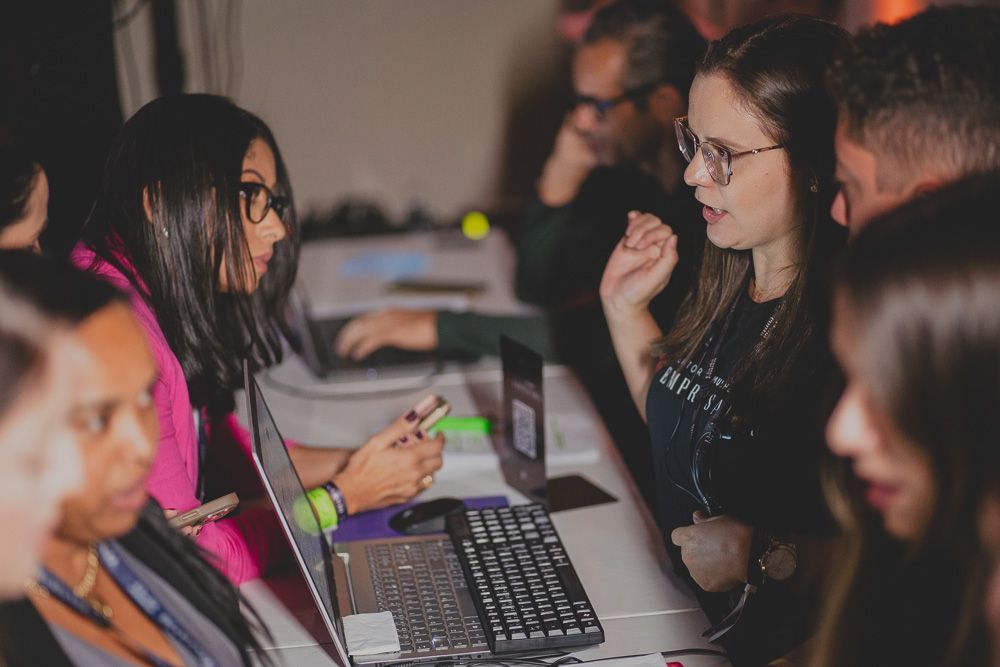 Um grupo de pessoas está sentado ao redor de uma mesa com laptops.
