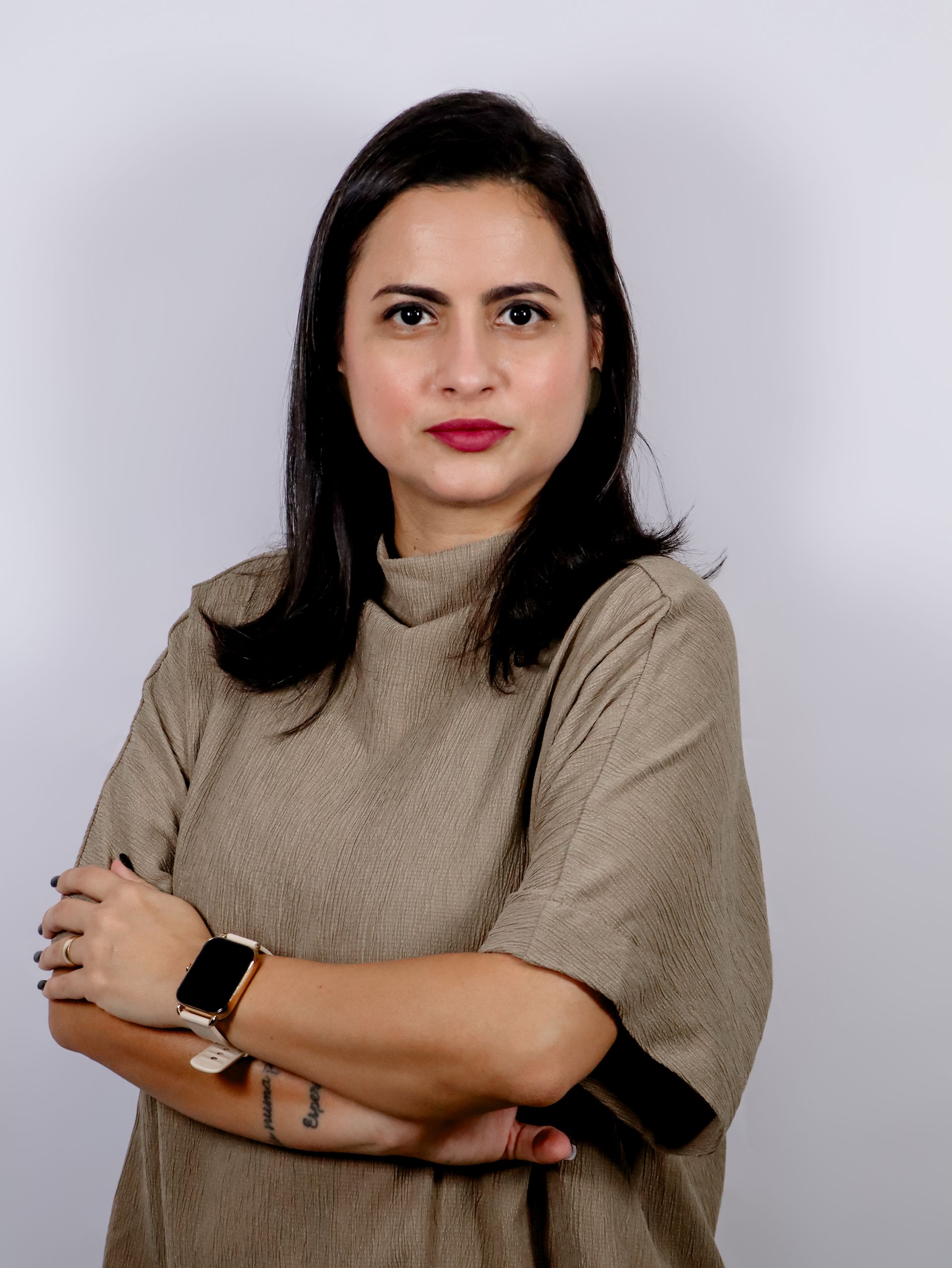 Uma mulher usando um relógio está parada com os braços cruzados.