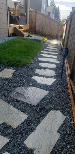 A stone walkway leading to a fence in a backyard.