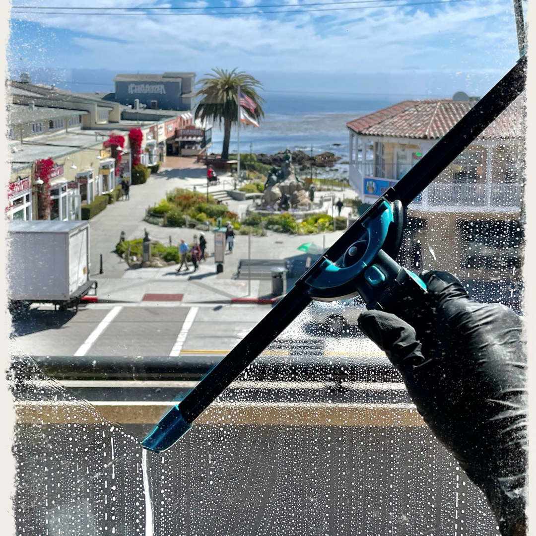 A person wearing blue gloves is cleaning a window with a squeegee.