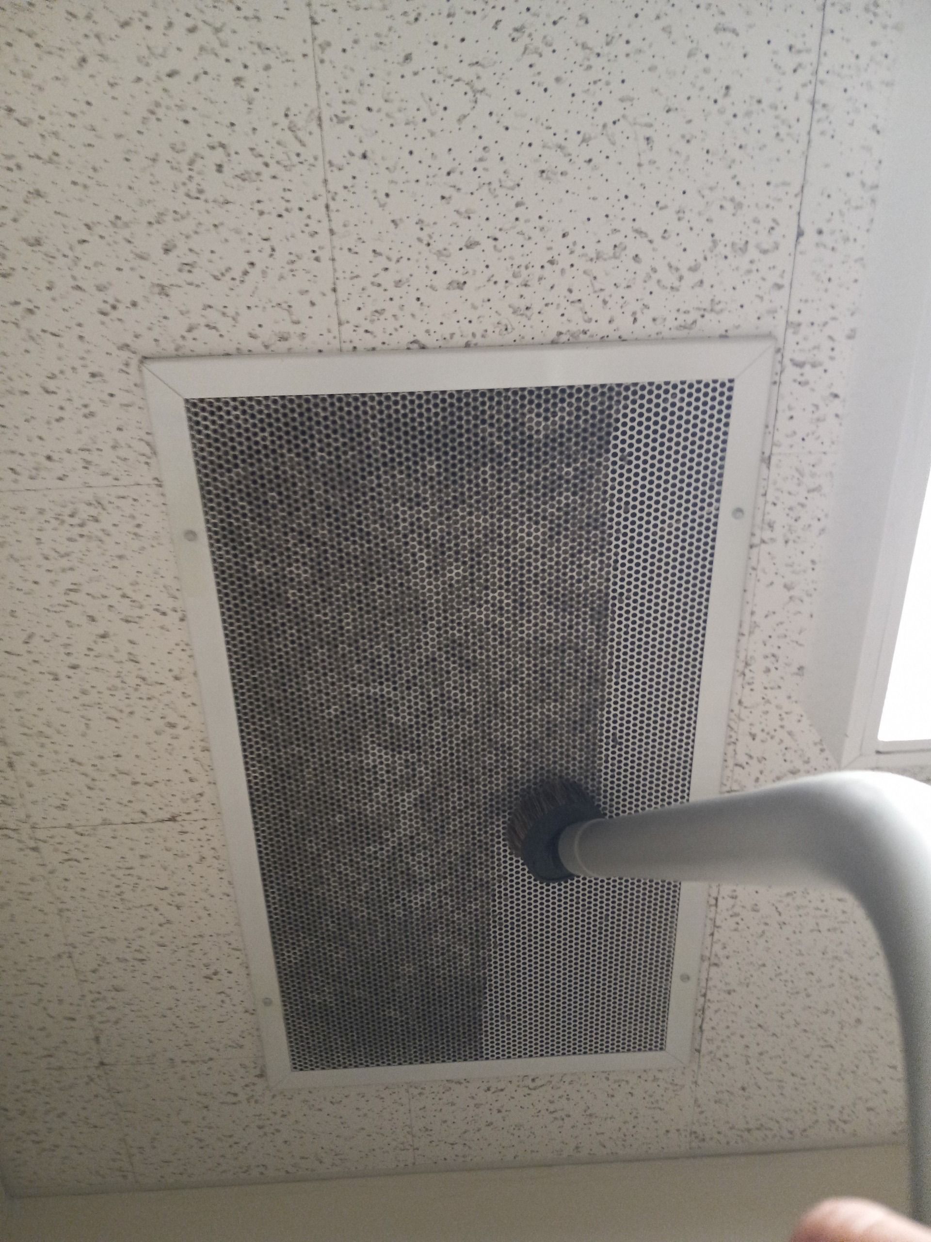 A person is cleaning a ceiling vent with a vacuum cleaner