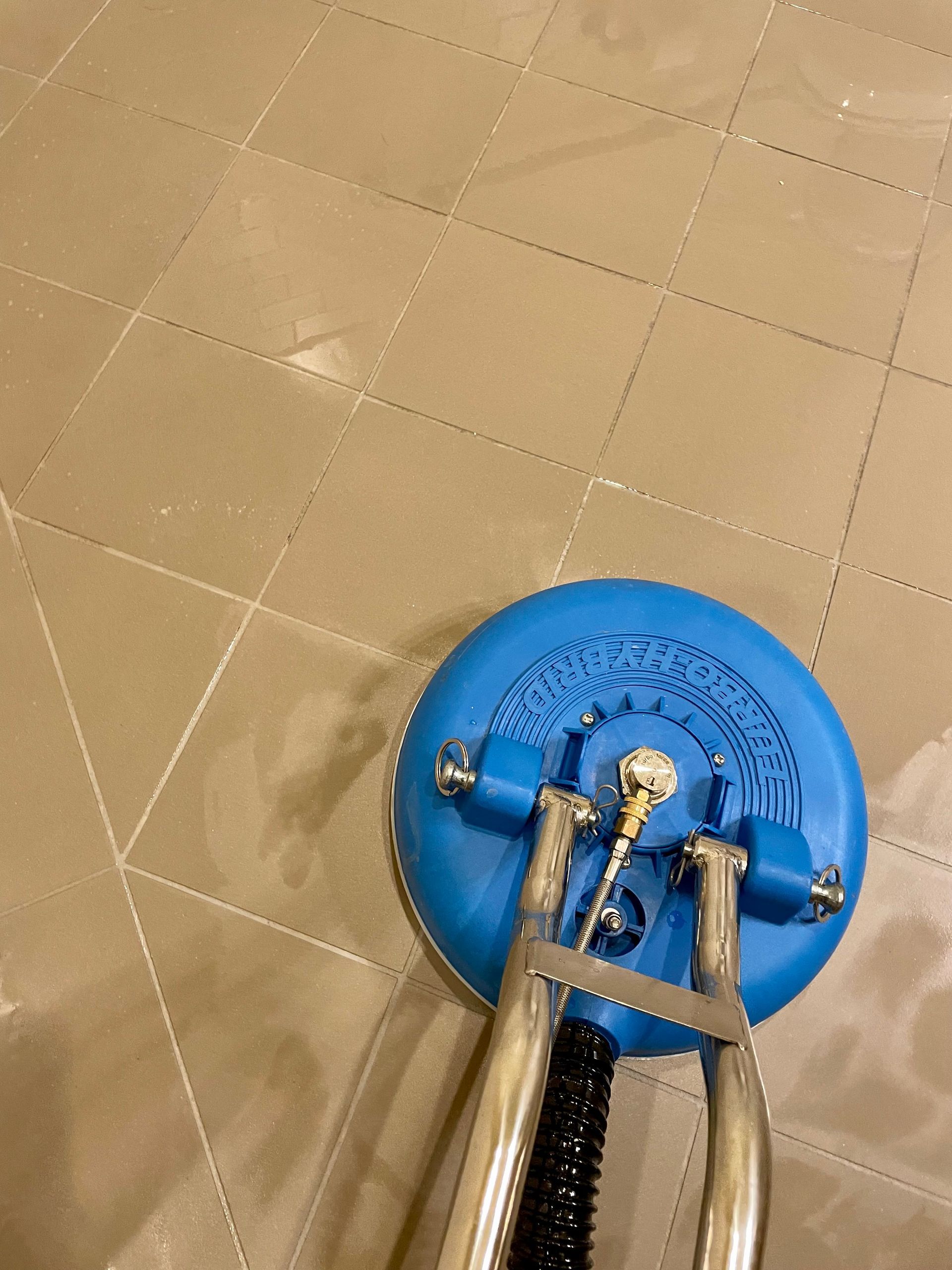 A blue vacuum cleaner is cleaning a tiled floor.