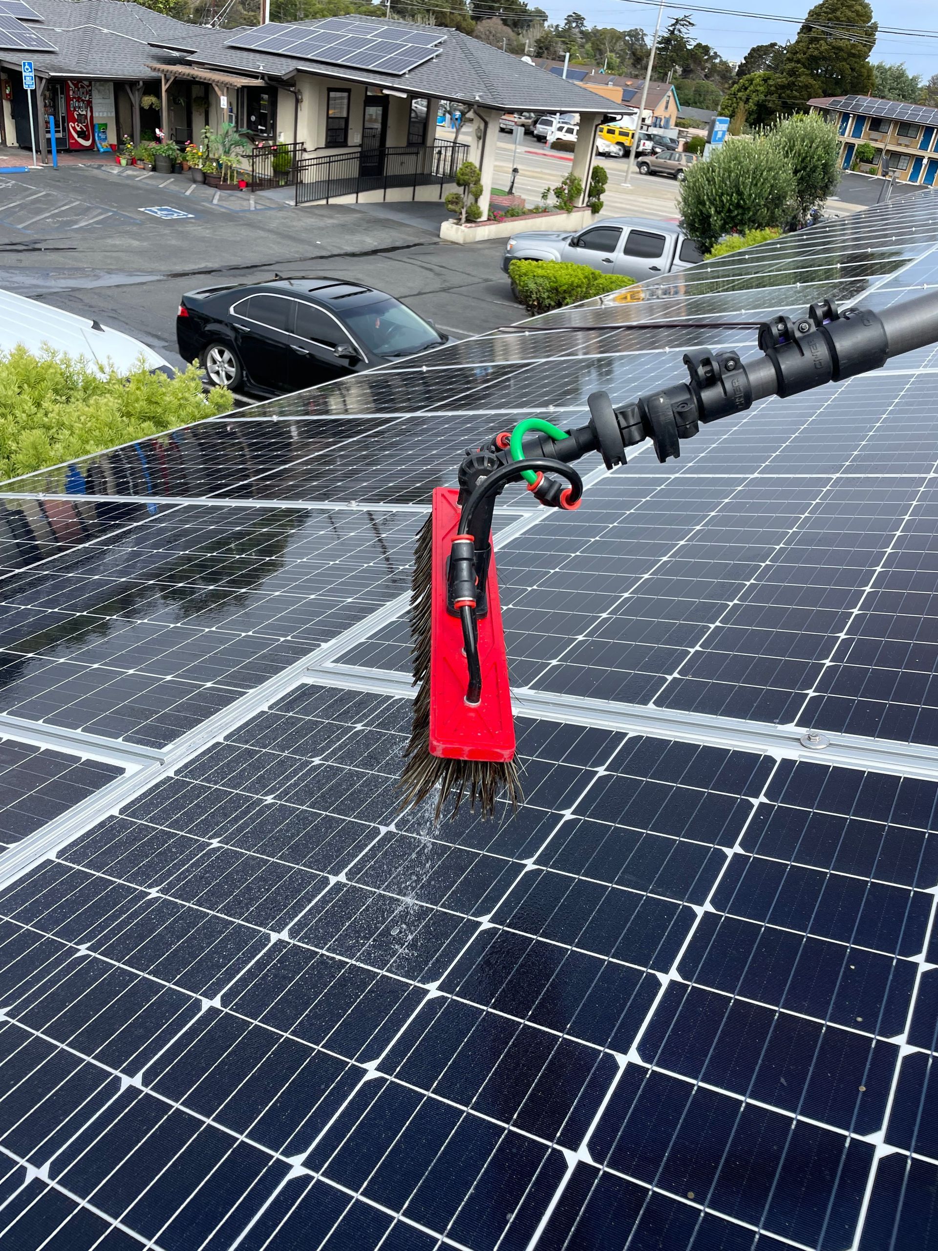 A man is cleaning solar panels on a roof with a broom.