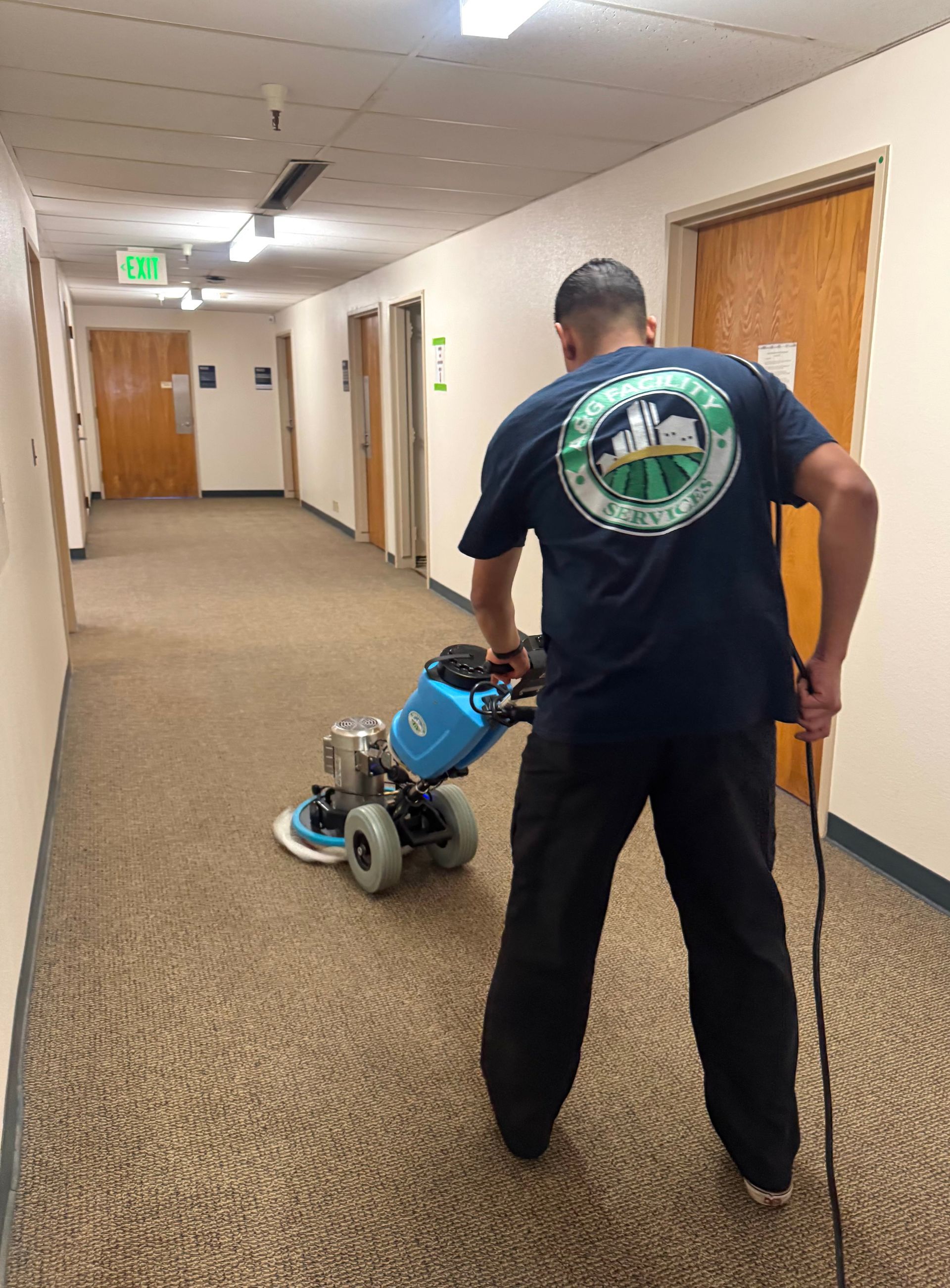 A man is cleaning the carpet in a hallway with a machine.