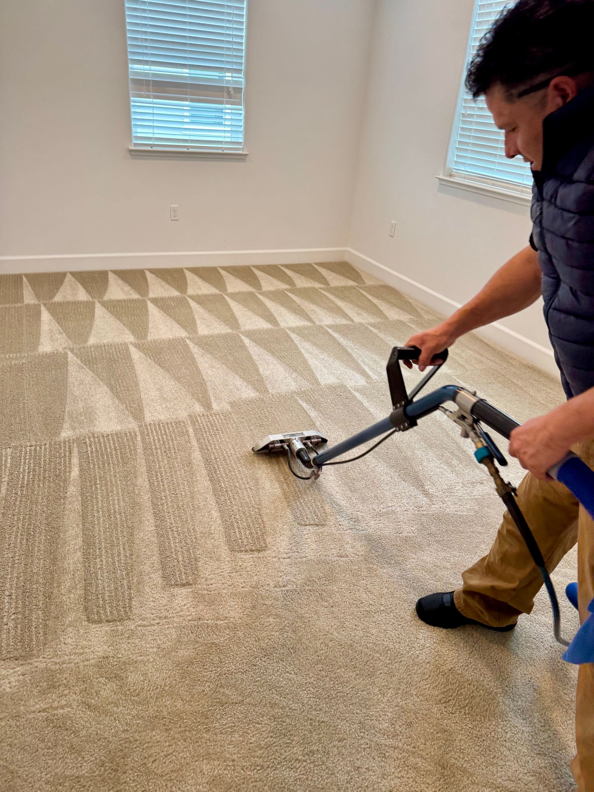 A man is cleaning a carpet with a vacuum cleaner in a room.