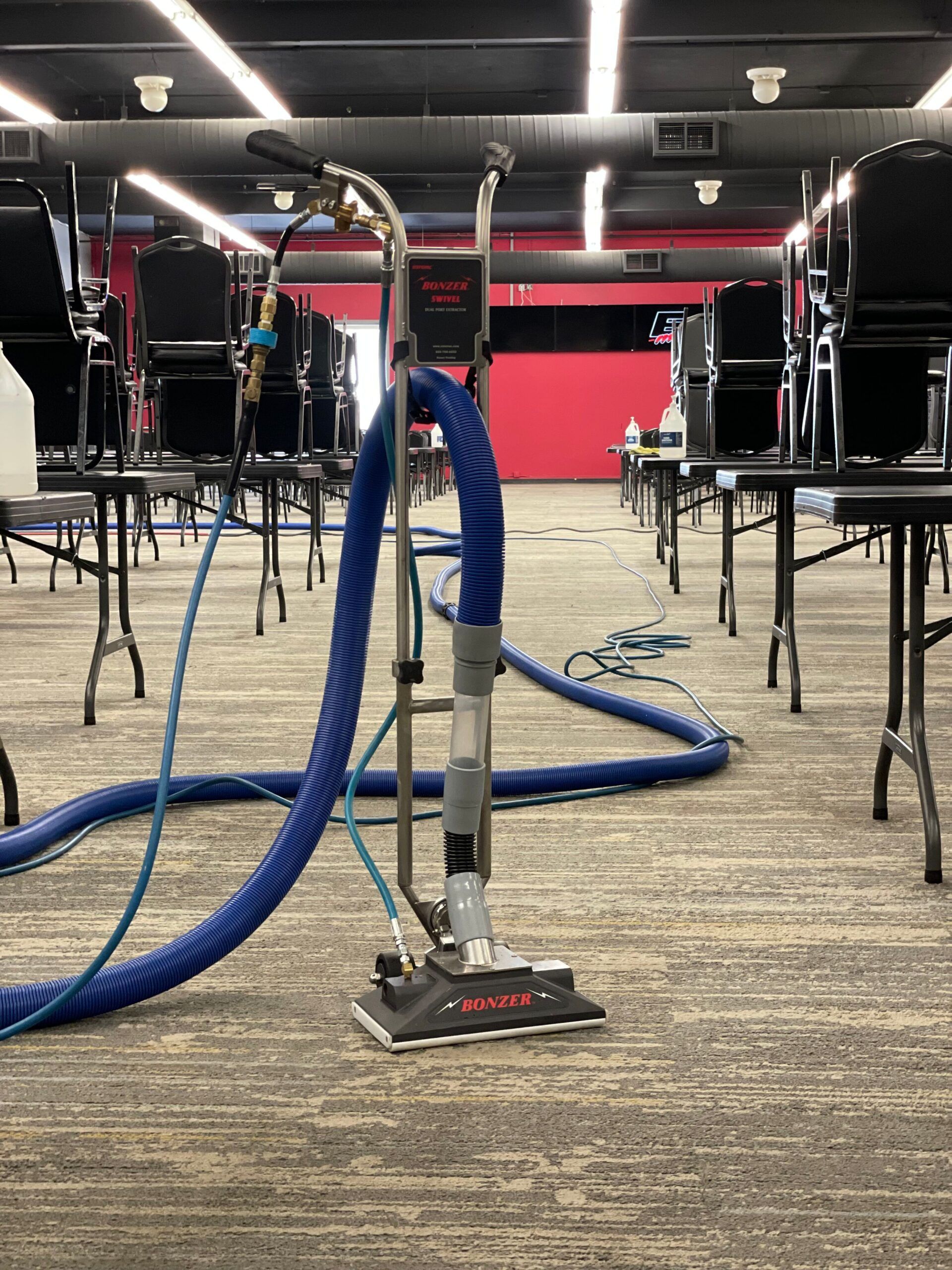 A vacuum cleaner is sitting on a carpet in a room with tables and chairs.