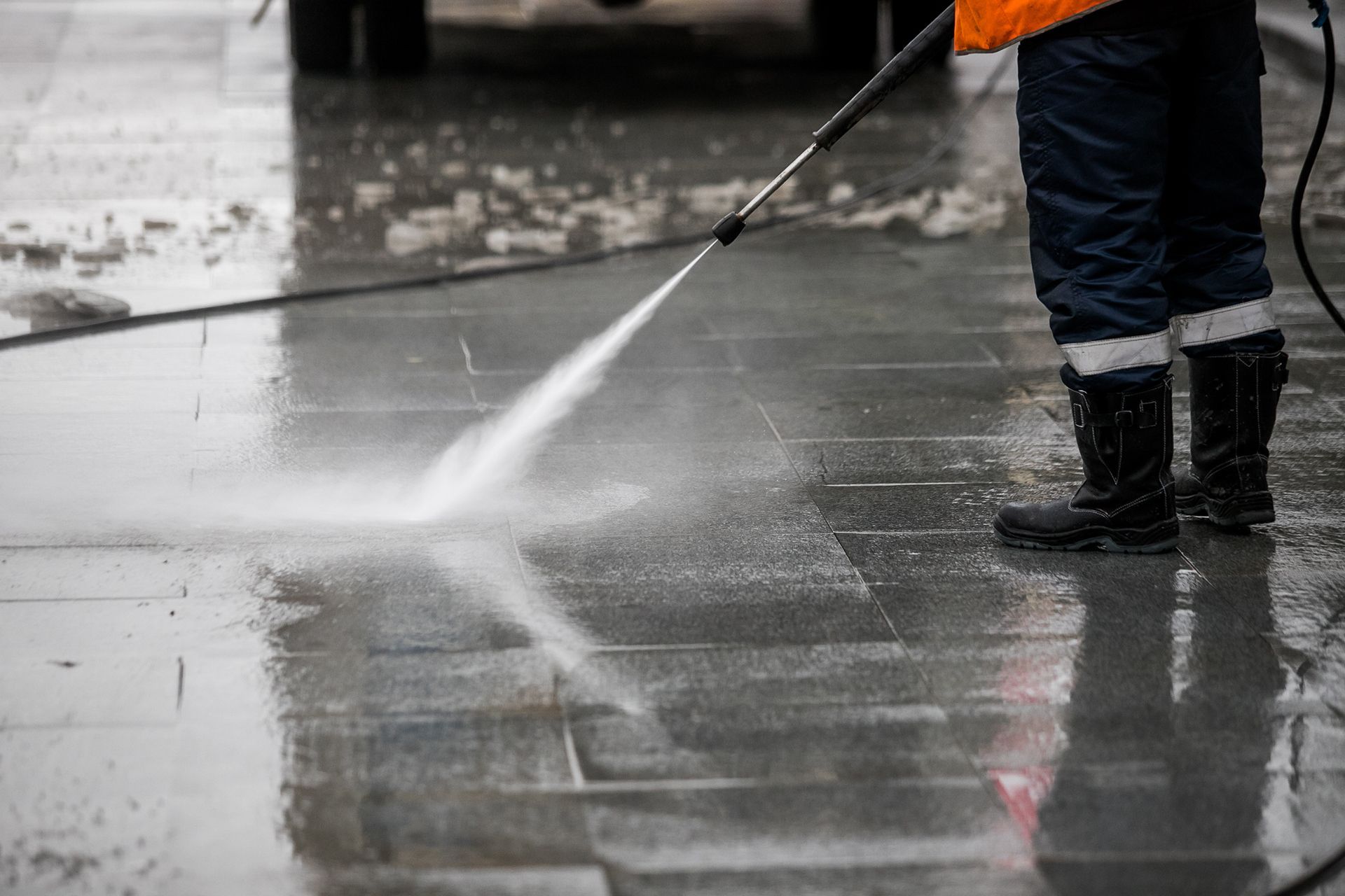 A man is using a high pressure washer to clean a sidewalk.
