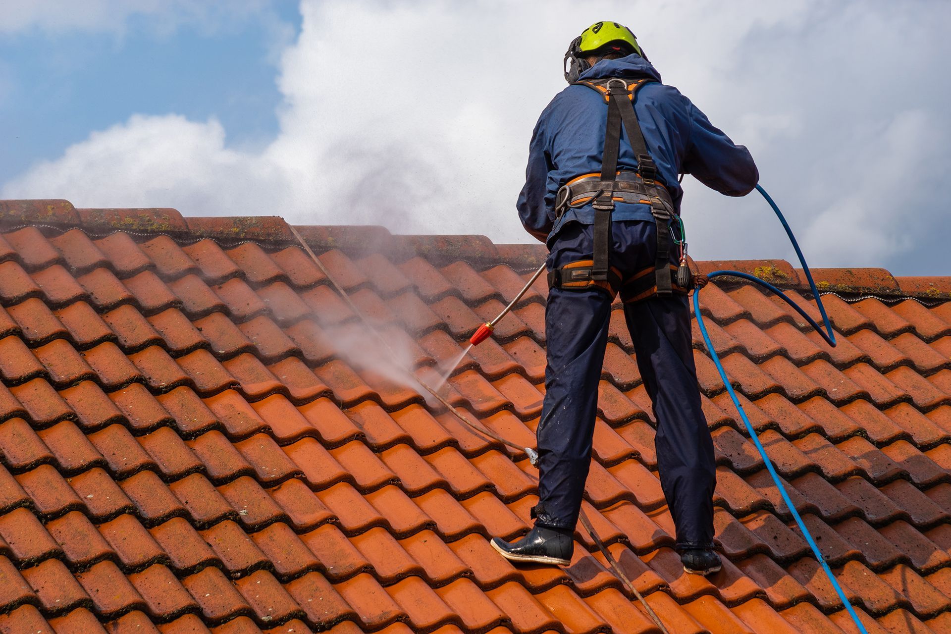 A man is cleaning a tiled roof with a high pressure washer.