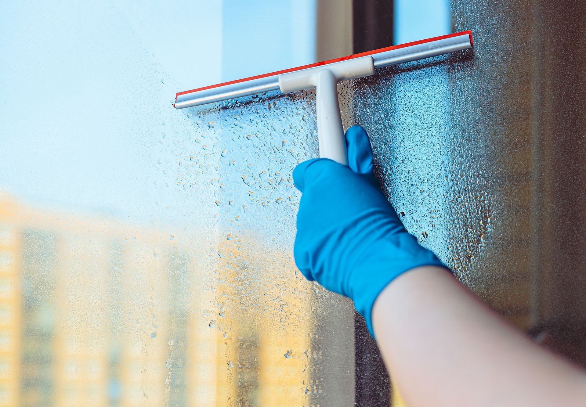 A person wearing blue gloves is cleaning a window with a squeegee.