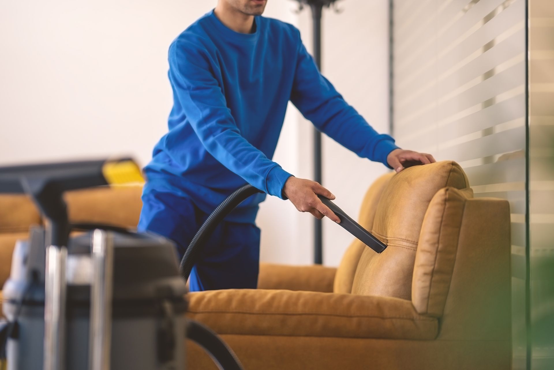 A man is cleaning a leather couch with a vacuum cleaner.