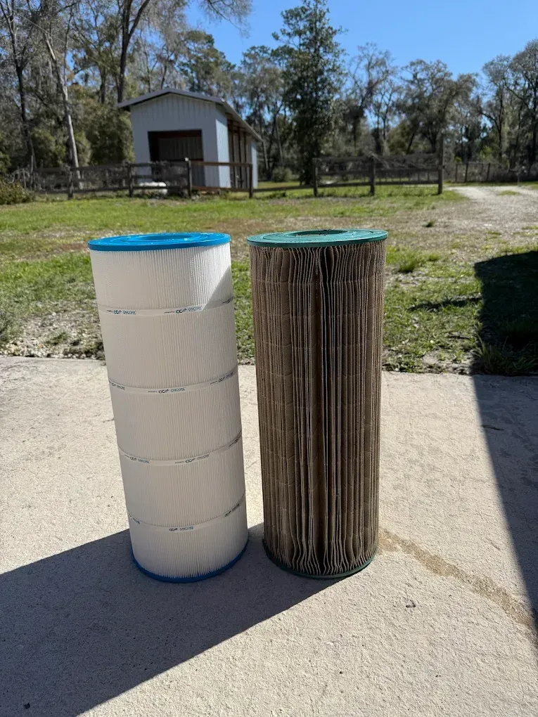 Two pool filters, one clean and white, the other dirty and brown, outdoors.