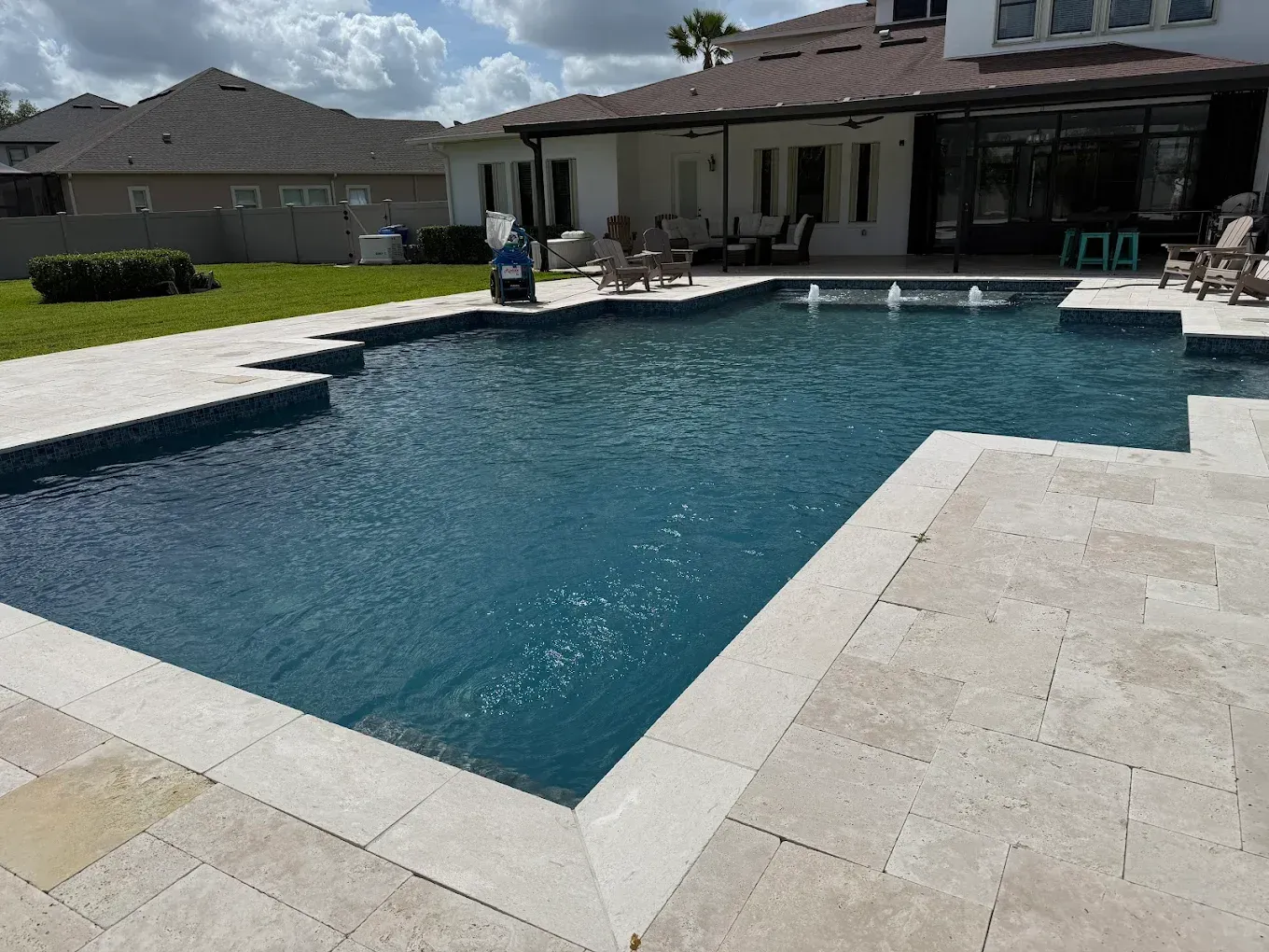 Swimming pool with blue water and stone patio, adjacent to a house with outdoor seating.