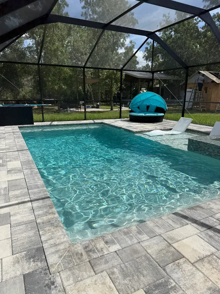 Pool with screen enclosure and surrounding pavers; teal seating and lounge chairs.