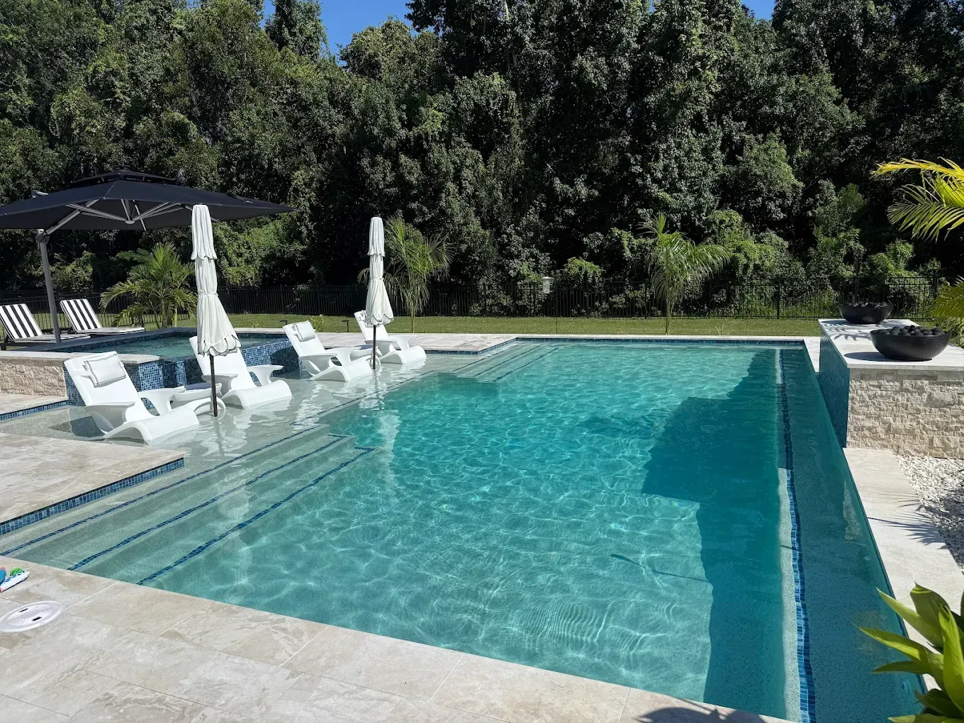 Pool with loungers and umbrellas; surrounded by trees on a sunny day.
