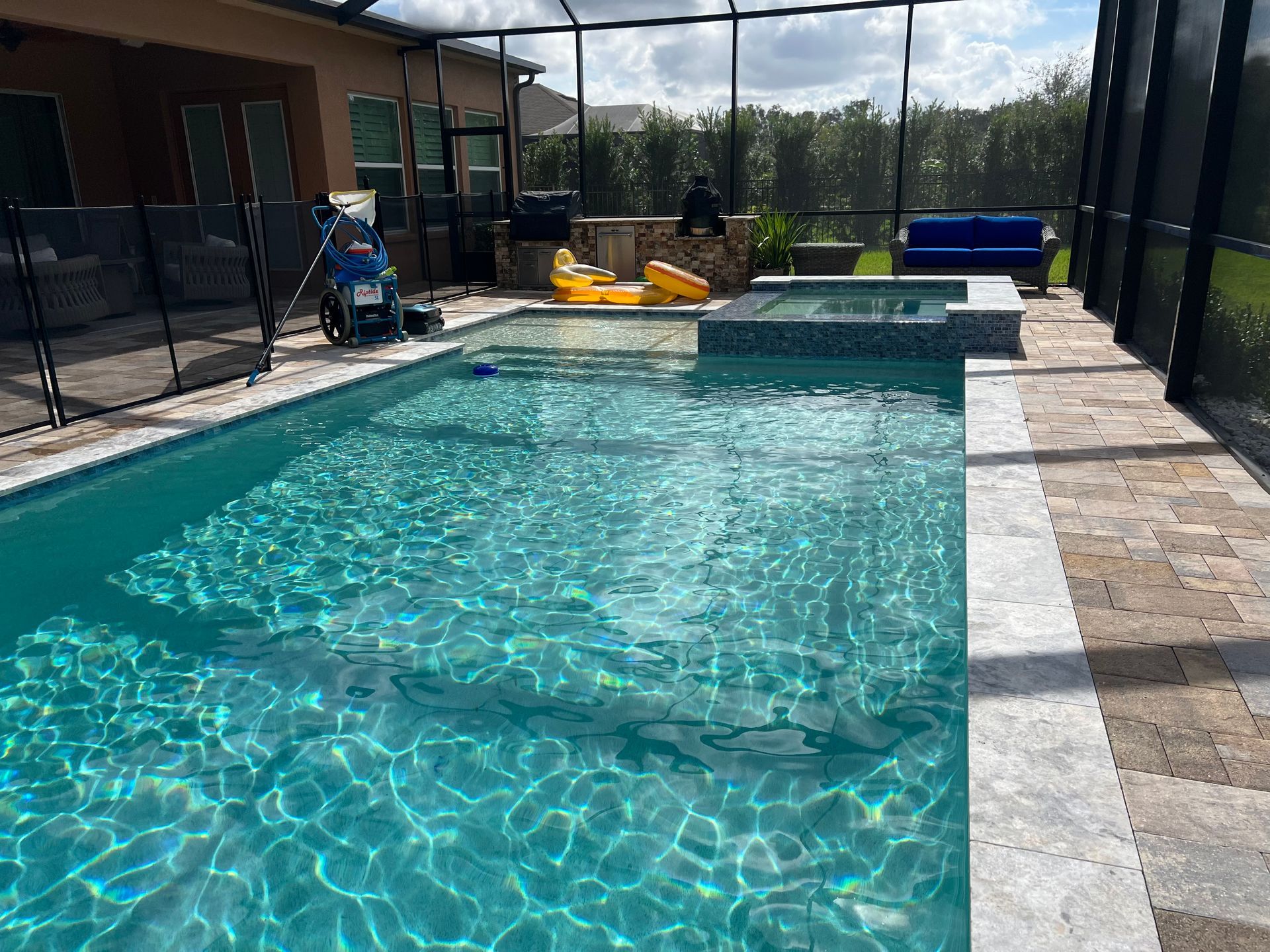 Swimming pool with blue water, tile deck, screen enclosure. Yellow float, pool equipment visible.