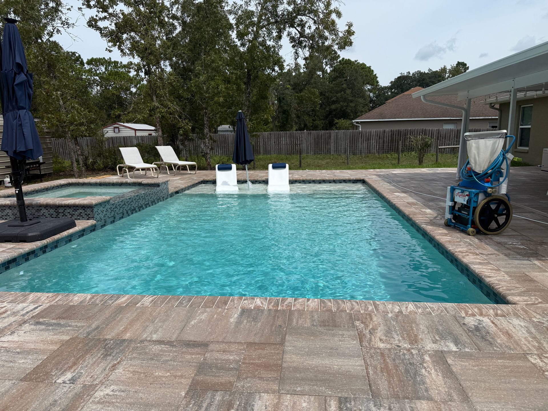 Swimming pool with a blue-tiled interior, surrounded by stone pavers, with a hot tub and lounge chairs.