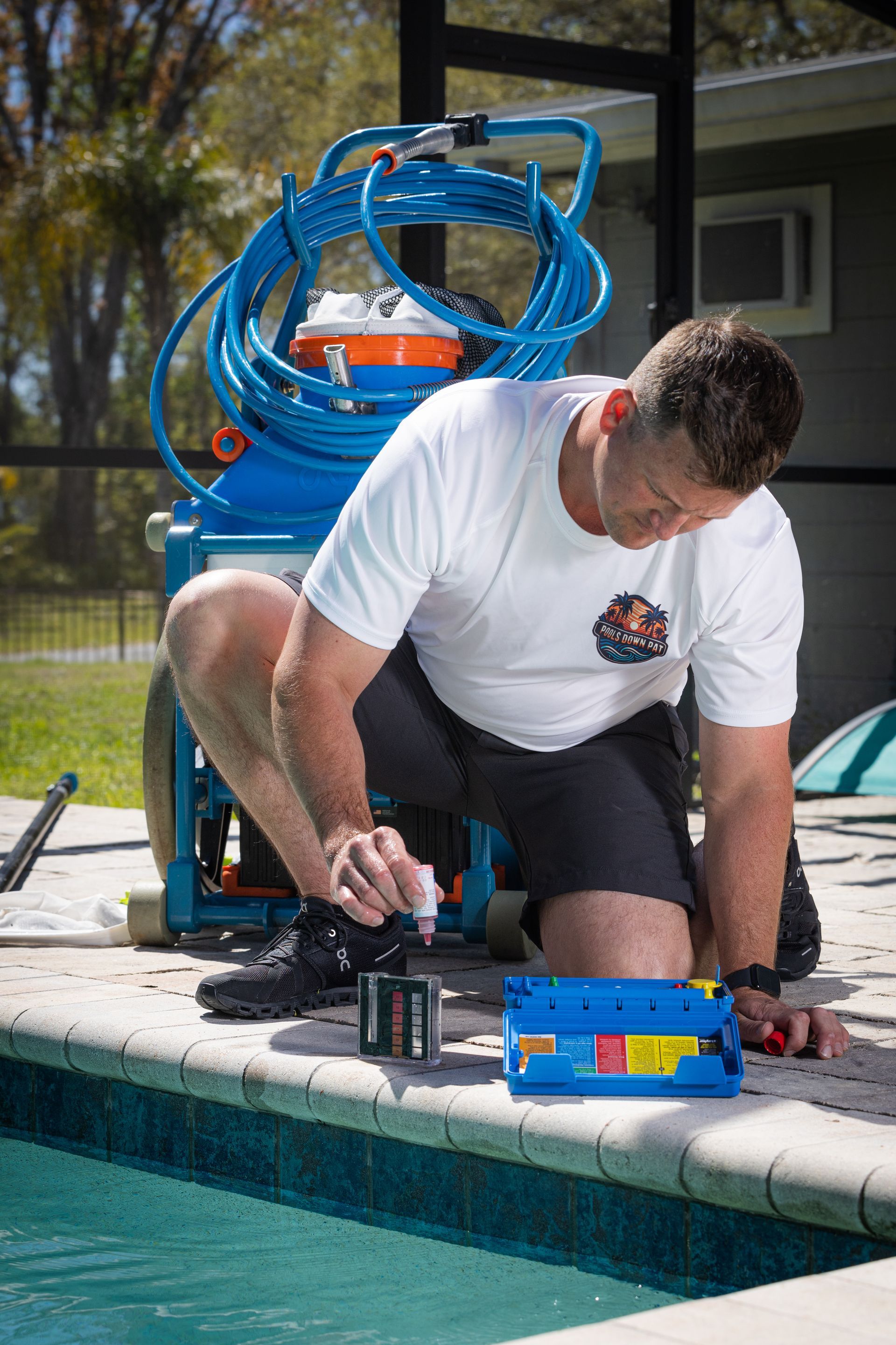 A hose , vacuum cleaner , and brush are sitting on the edge of a swimming pool.