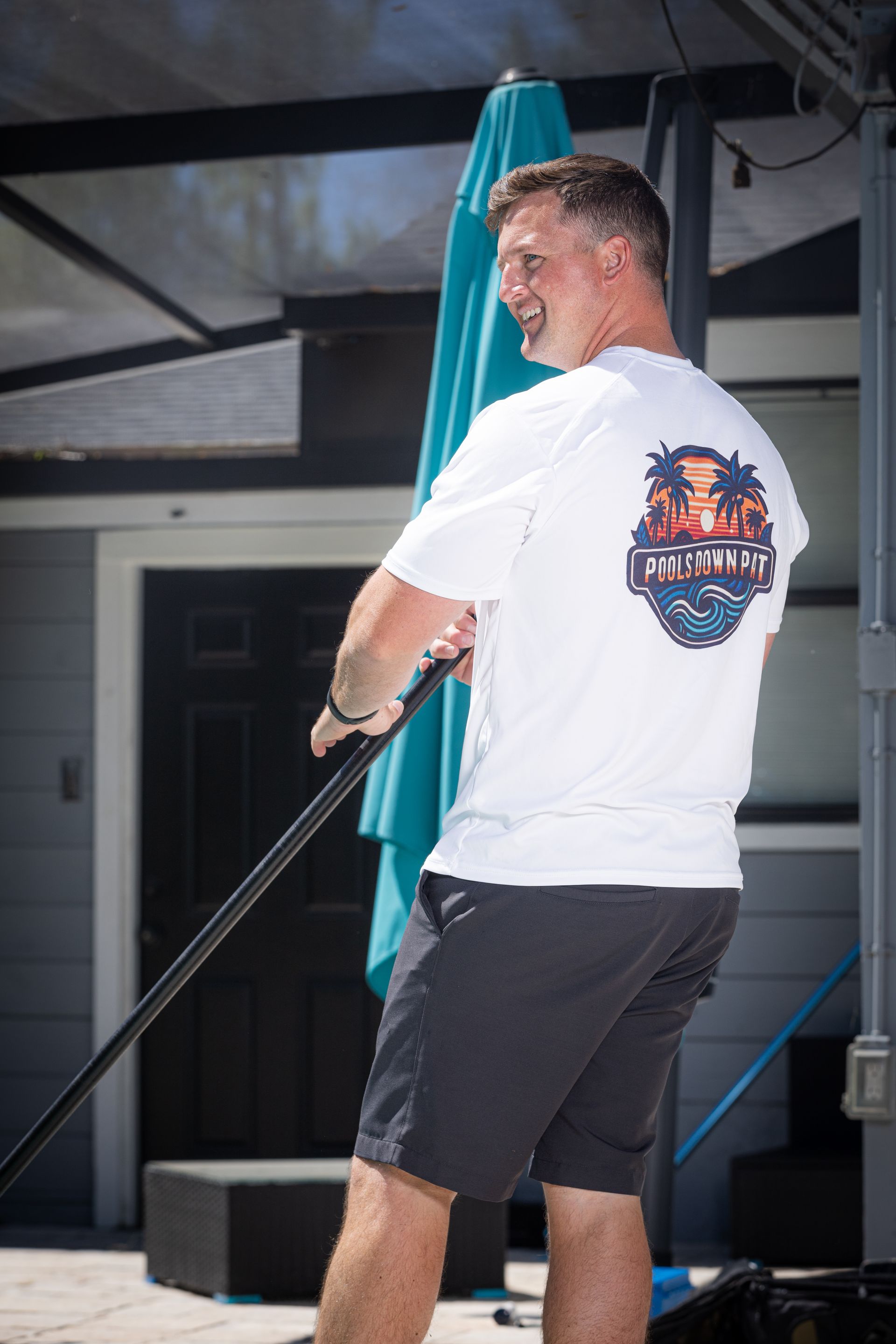Man in white shirt with graphic, pulling on black pole outside.