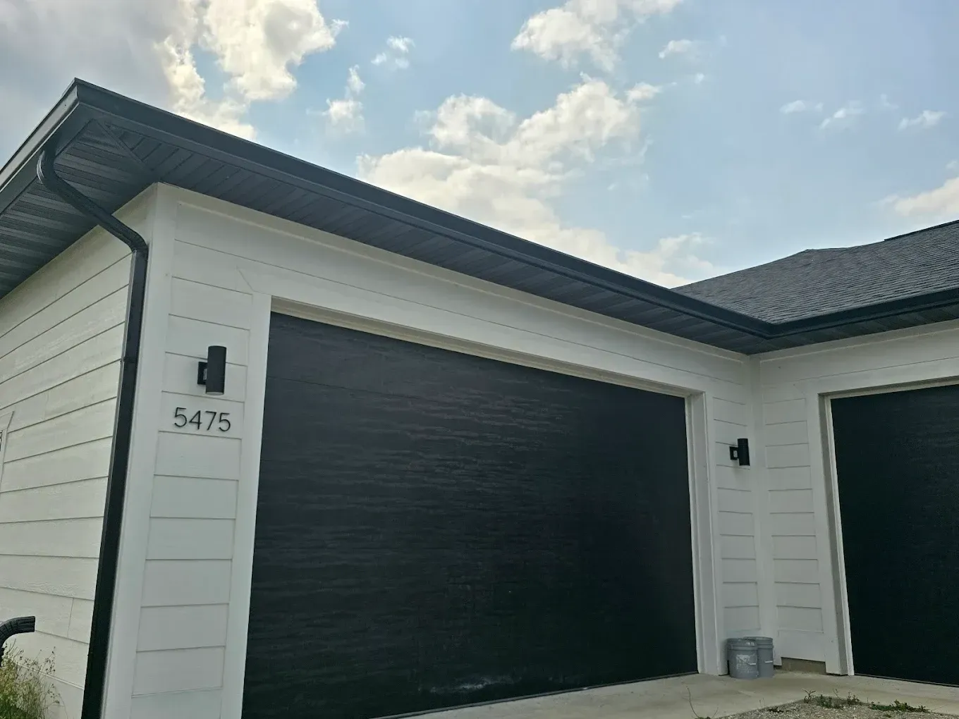 A white house with black garage doors and a black gutter.