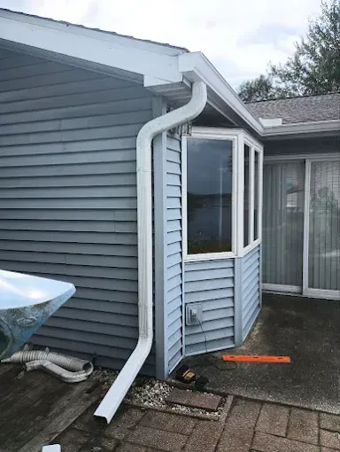 Exterior view of a house with blue siding and white gutters, featuring a bay window and a downspout.