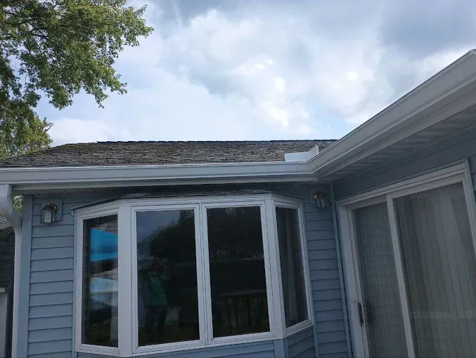 Blue house with white trim, bay window, and sliding glass door. Cloudy sky above.