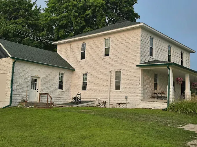 Two-story white house with a porch and attached garage, green roof and trim. Green lawn in front.