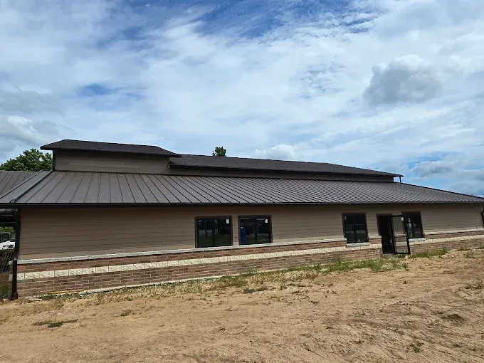 Tan building with brown roof and windows against a cloudy blue sky.