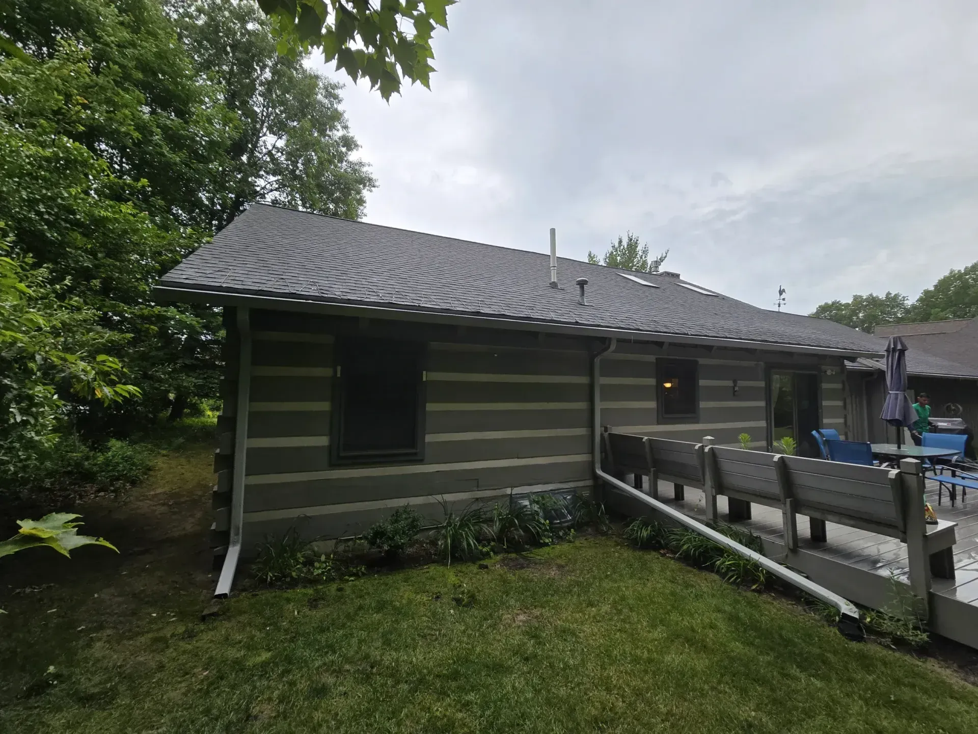 Log cabin with dark roof and trim, surrounded by green grass and trees.
