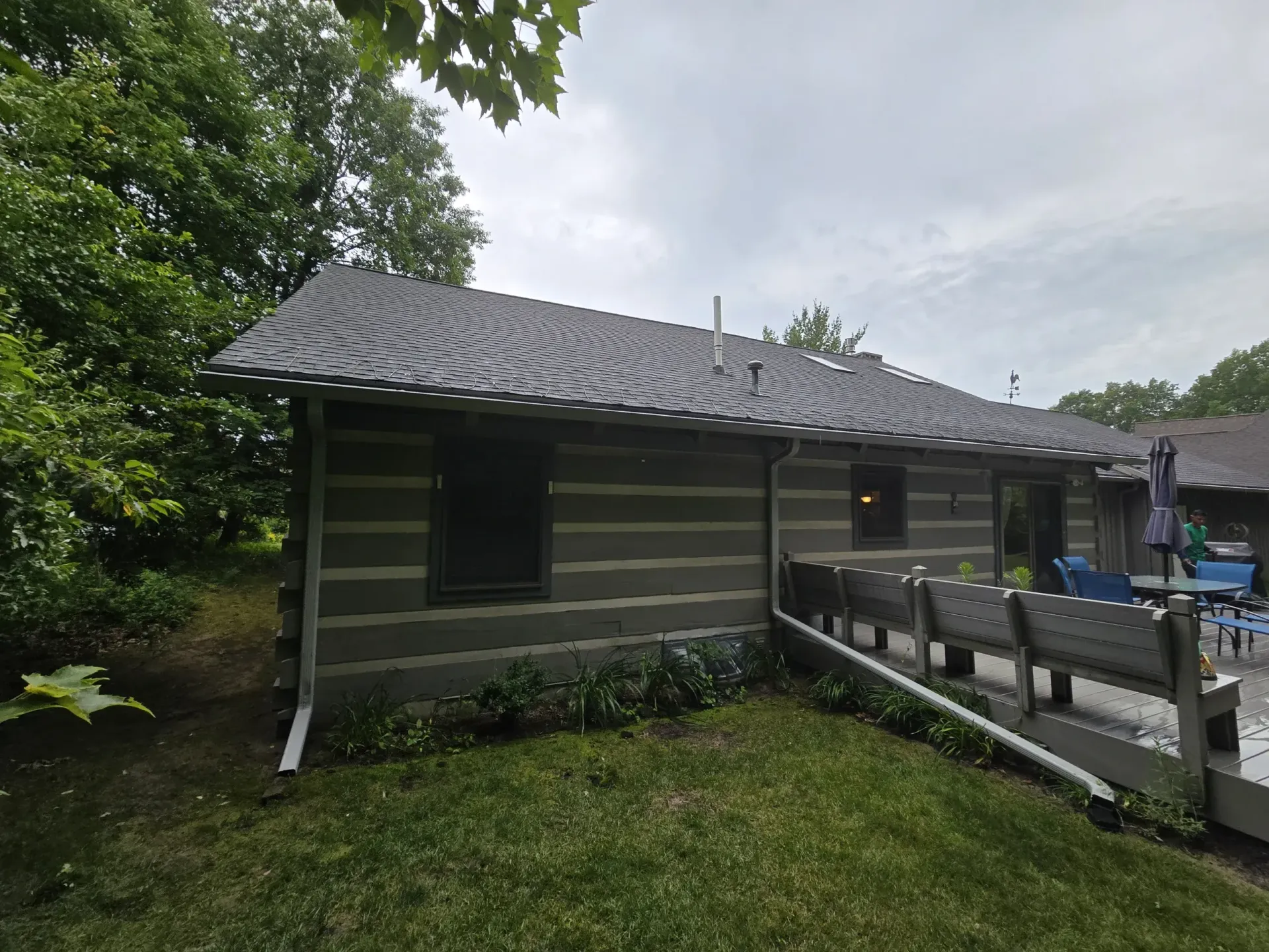A log cabin with a gray roof and a deck in the backyard.