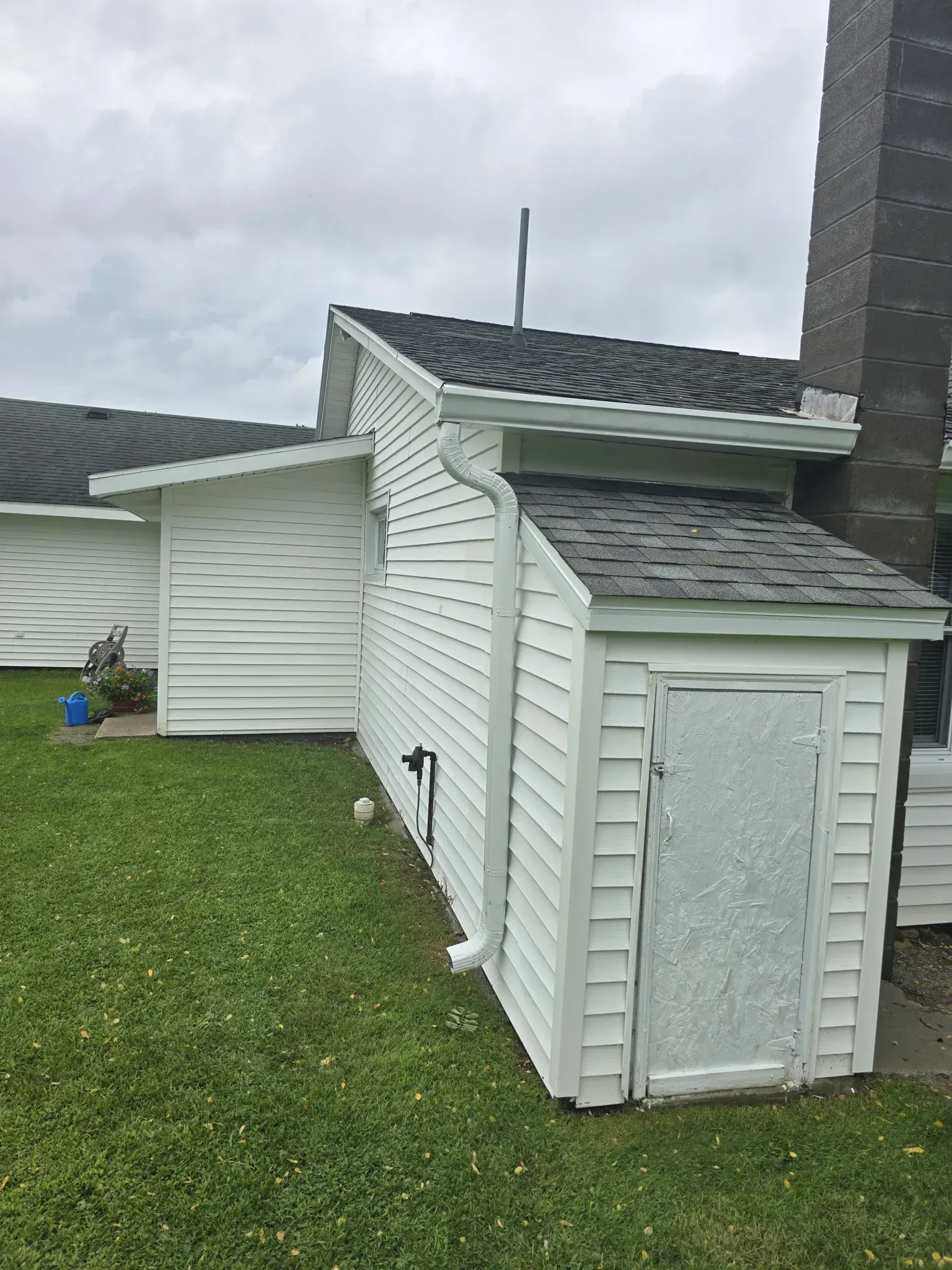 A white shed is sitting in the grass next to a house.