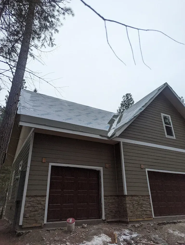 Two-story building with green siding and brown garage doors, grey roof. Stone accents.