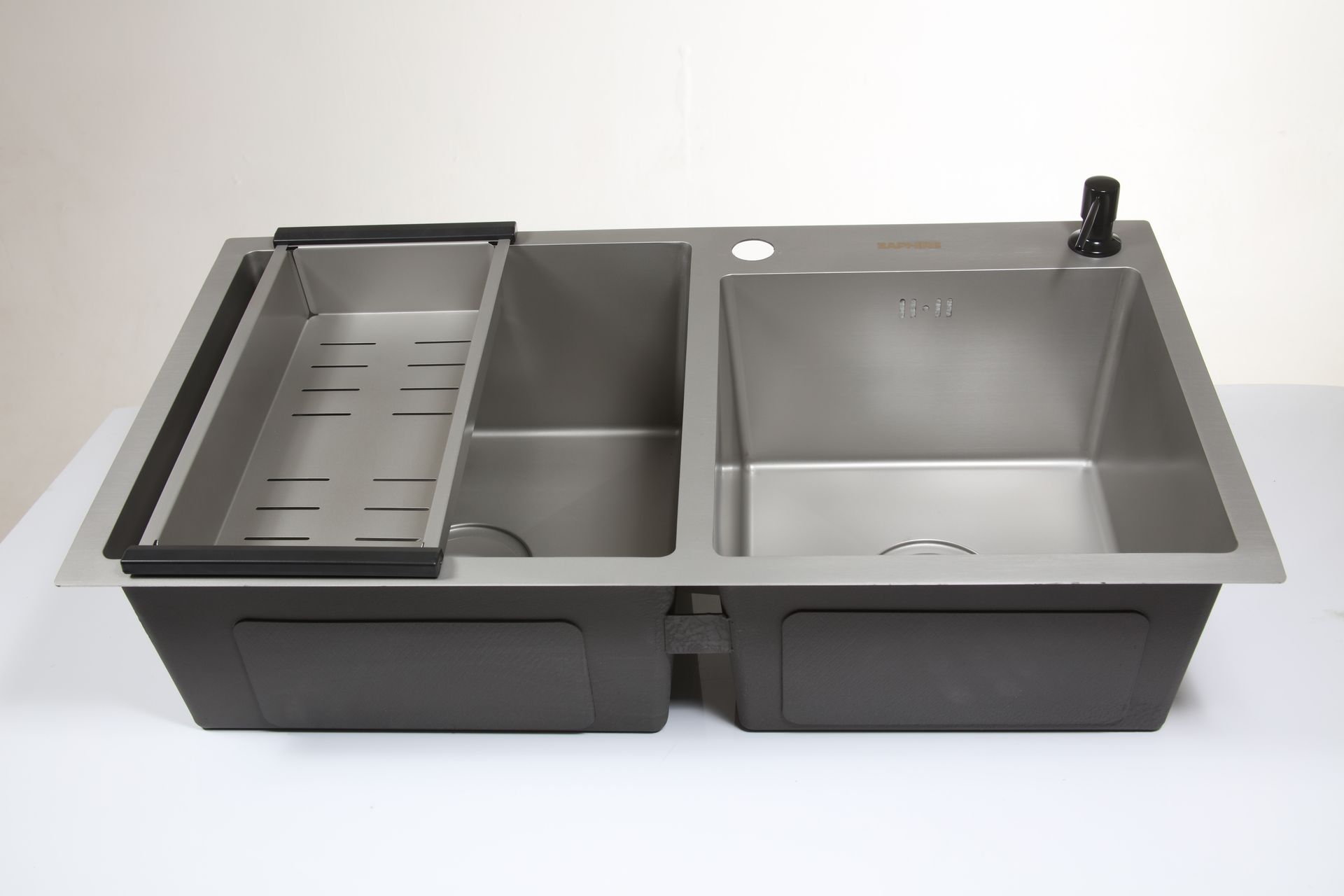 Fregadero de cocina de acero inoxidable con escurridor, grifo y dispensador de jabón integrados. Instalado sobre una encimera blanca.